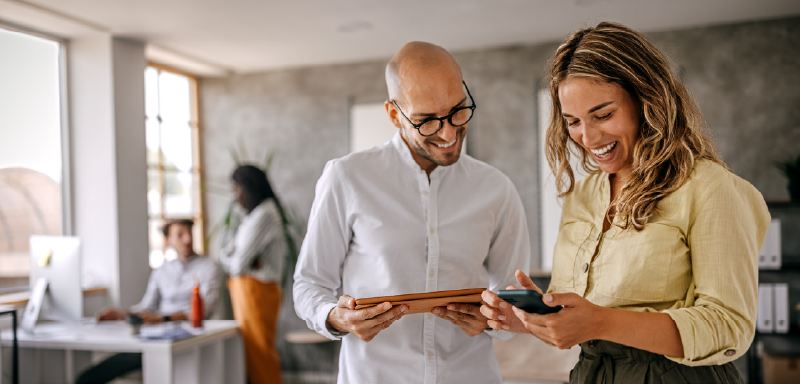 Colleagues in a modern office collaborating using mobile devices and digital tools, representing Woodhull’s innovative approach to document management and technology solutions.