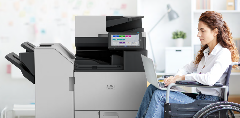 Professional using a laptop next to a Ricoh multifunction printer, highlighting Woodhull’s accessible and inclusive office technology solutions for diverse work environments.