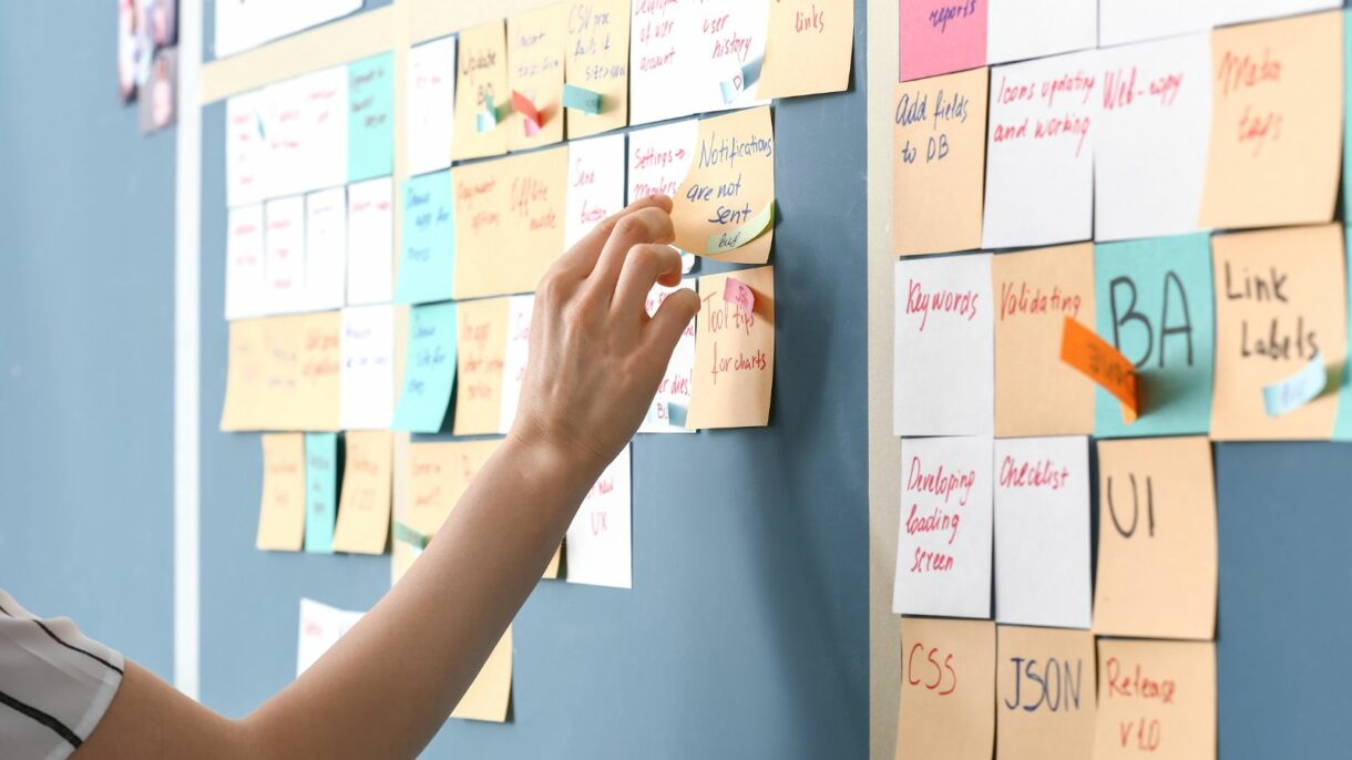 Close-up of a hand organizing colorful sticky notes on a project planning board, illustrating Woodhull’s structured approach to innovation and collaboration as a WBENC-certified business.