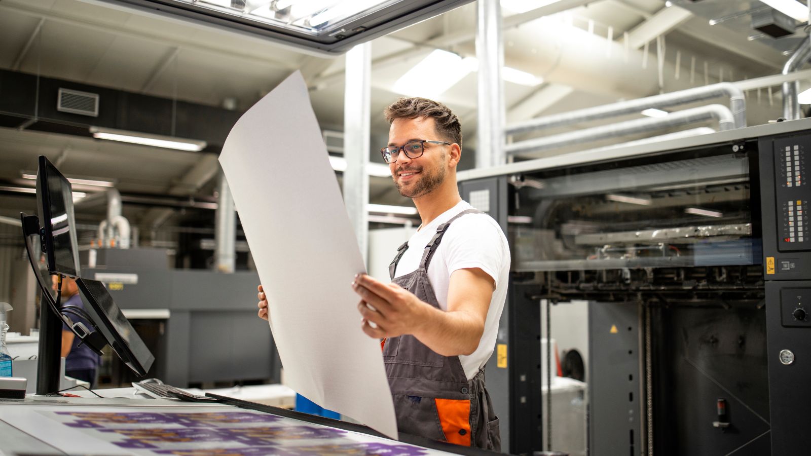 Smiling technician reviewing a printed sheet at Woodhull, LLC, demonstrating cutting-edge production printing technology for businesses in Ohio.